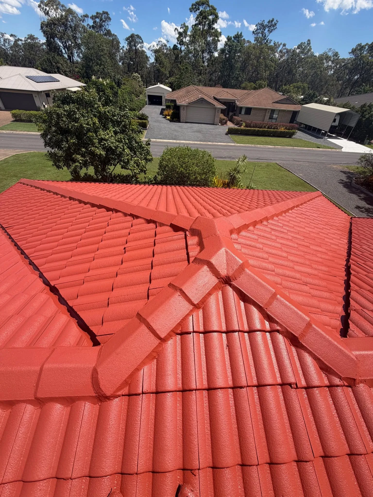 Aerial view of a hip and ridge intersection on a freshly painted Manor Red tile roof, with a suburban street visible below