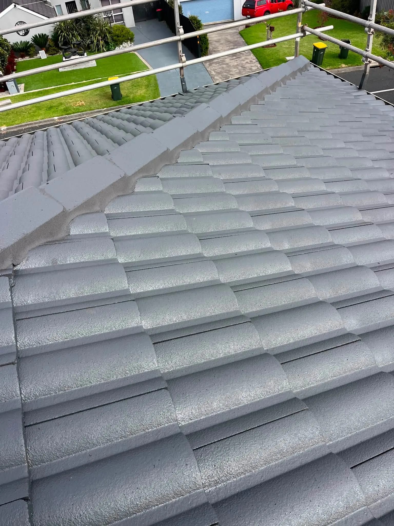 Rooftop view of a freshly restored roof in Monument grey along the ridge line, with scaffolding and a front garden visible below