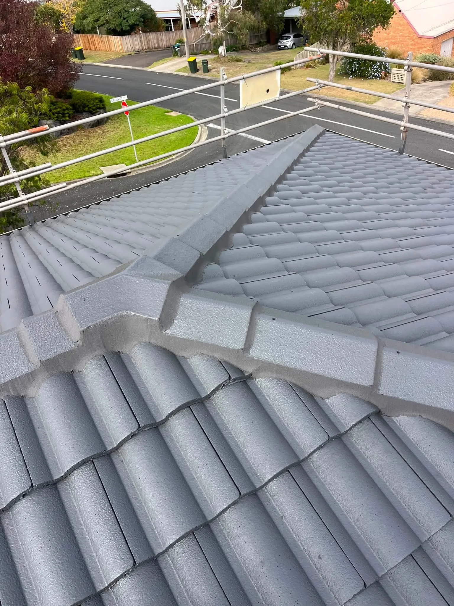 Rooftop view of a hip junction on a freshly restored Monument-grey tile roof, overlooking a suburban street corner