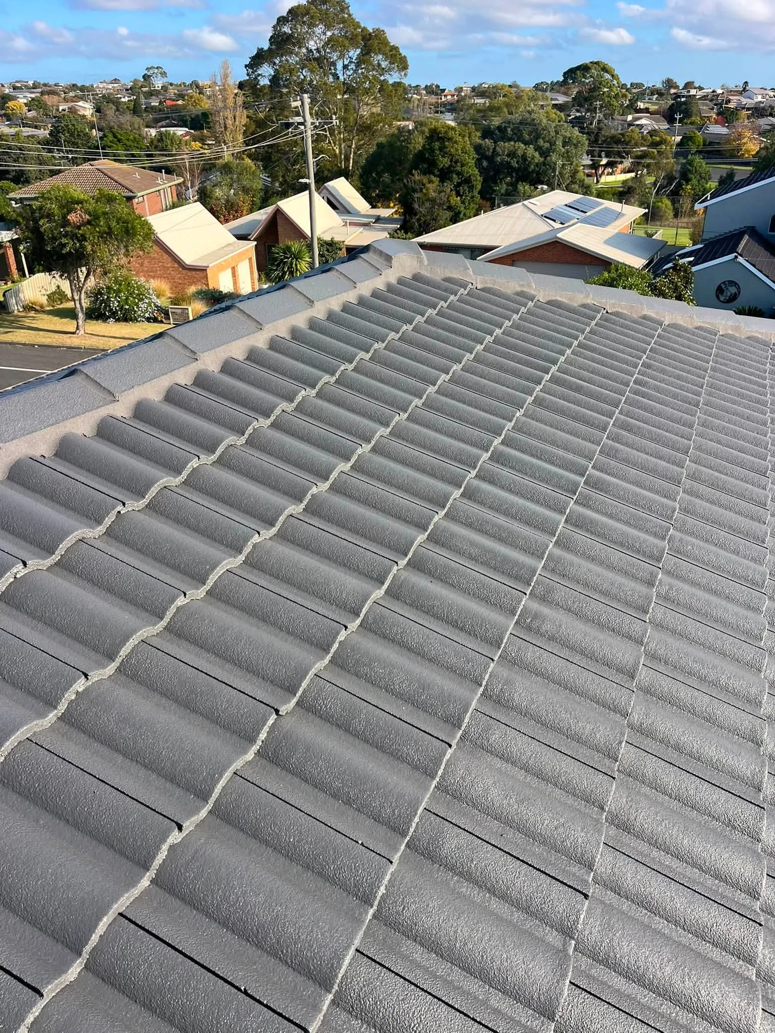 Rooftop view along the ridge of a freshly restored Monument-grey tile roof, overlooking a residential street
