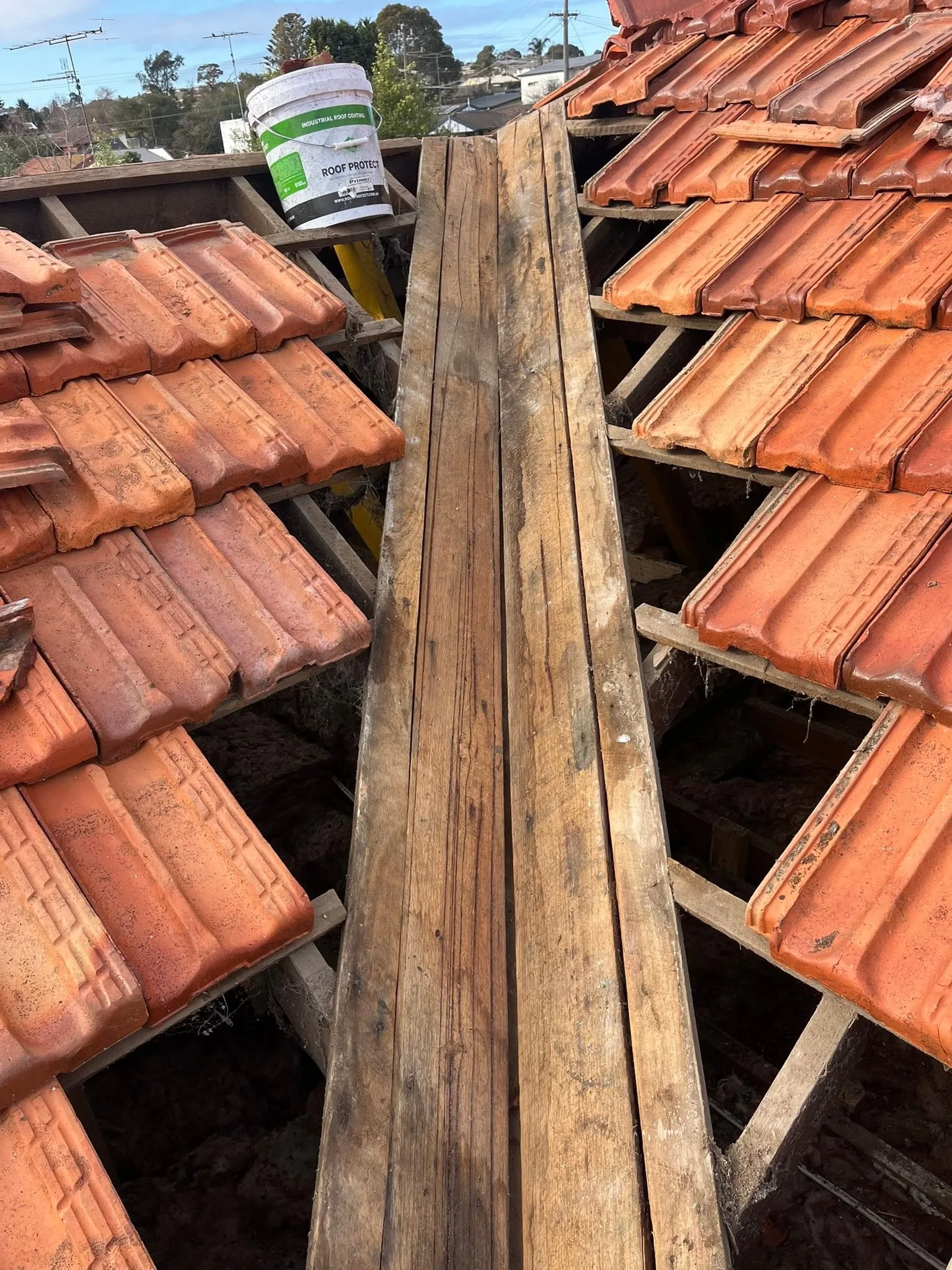 New valley boards being fitted between sections of terracotta tile roof, with a roof coating primer tin visible nearby